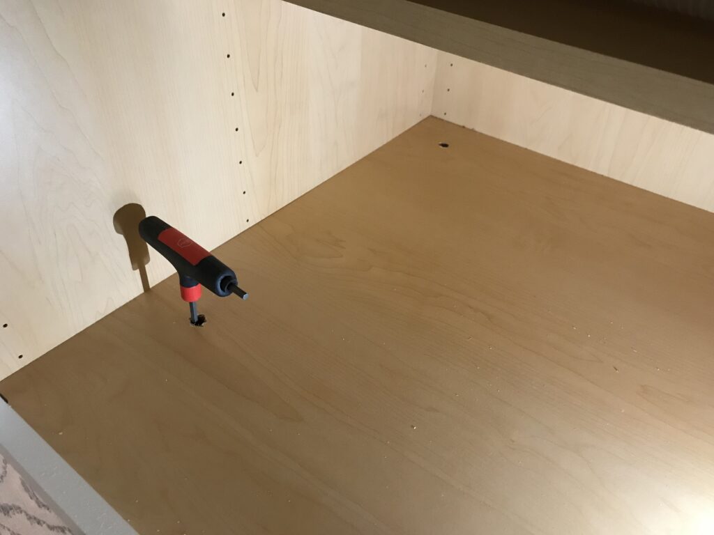 Showing the holes in the cabinet shelf where the leveling foot is adjusted.